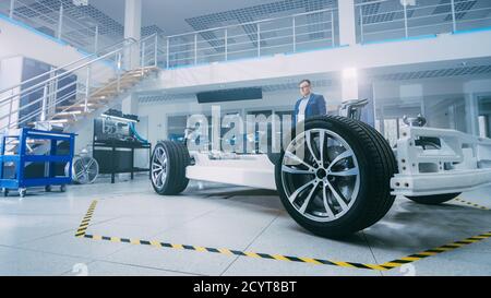 Automotive Design Engineer Looking at Electric Car Chassis Prototype. In Innovation Laboratory Facility Concept Vehicle Frame Includes Wheels, Engine Stock Photo