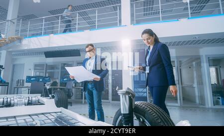 Automotive Design Engineers Looking at Technical Drawings of a Electric Car Chassis Prototype. In Innovation Laboratory Facility Concept Vehicle Frame Stock Photo