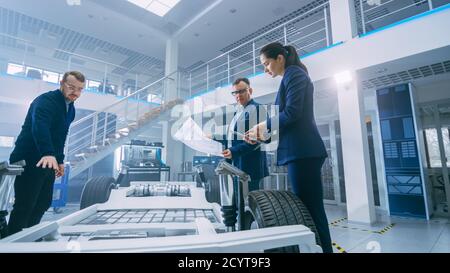 Automotive Design Engineers Looking at Technical Drawings of a Electric Car Chassis Prototype. In Innovation Laboratory Facility Concept Vehicle Frame Stock Photo