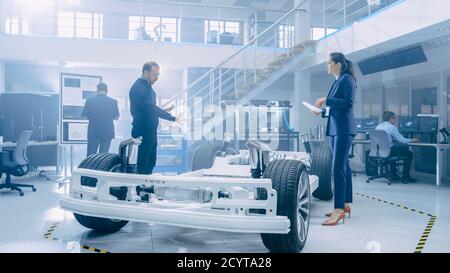 Automotive Design Engineers Looking at Technical Drawings of a Electric Car Chassis Prototype. In Innovation Laboratory Facility Concept Vehicle Frame Stock Photo