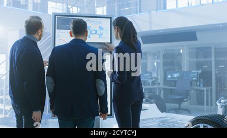 Diverse Team of Design Engineers are Working and Discussing Something on a Interactive Whiteboard Next to an Electric Car Chassis Prototype. In High Stock Photo