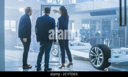 Diverse Team of Design Engineers are Working and Discussing Something on a Interactive Whiteboard Next to an Electric Car Chassis Prototype. In High Stock Photo