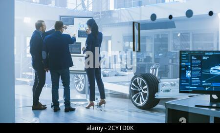 Diverse Team of Design Engineers are Working and Discussing Something on a Interactive Whiteboard Next to an Electric Car Chassis Prototype. In High Stock Photo
