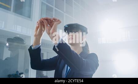 Female Engineer Using Augmented Reality Headset Making Gestures of working with Virtual Objects in the Air. In Innovation High Tech Laboratory Stock Photo