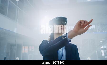 Female Engineer Using Augmented Reality Headset Pushes Virtual Buttons in the Air. In Innovation High Tech Laboratory Facility with Futuristic Stock Photo