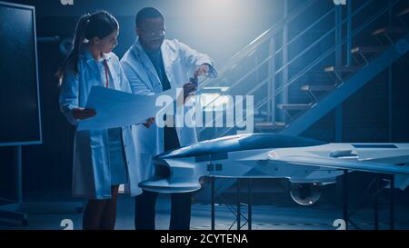 Two Aerospace Engineers Work On Unmanned Aerial Vehicle Drone Prototype. Aviation Scientists in White Coats Holding Blueprints. Laboratory with Stock Photo