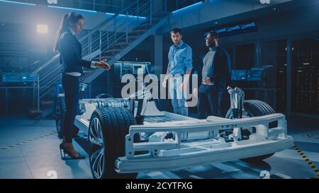 International Team of Automobile Design Engineers Discussing Design of Autonomous Electric Car Prototype. Vehicle Platform Chassis With Wheels Stock Photo