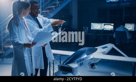 Two Aerospace Engineers Work On Unmanned Aerial Vehicle Drone Prototype. Aviation Scientists Talking, using Blueprints. Industrial Laboratory with Stock Photo