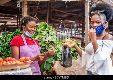 woman selling to a customer in a local market, both wearing face mask wrongly Stock Photo