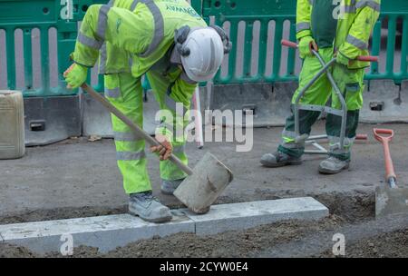 A workman seen using a wooden mallet to put a new  piece of curb in its place. Stock Photo