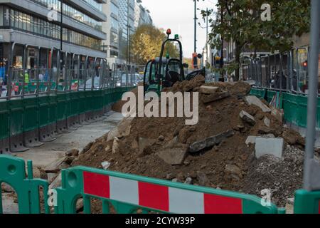 A pile of soil and rubble seen on the side of a street with an excavator in the background. Stock Photo