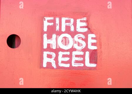 Fire-fighting table with inscription by white paint Fire Hose Reel on a red wall background with the hole, copy space. Stock Photo
