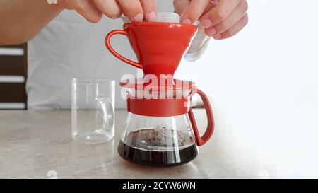 Man brews at home v 60. He puts paper filter in ceramic dripper and pours hot water, preparing filter for pouring coffee Stock Photo