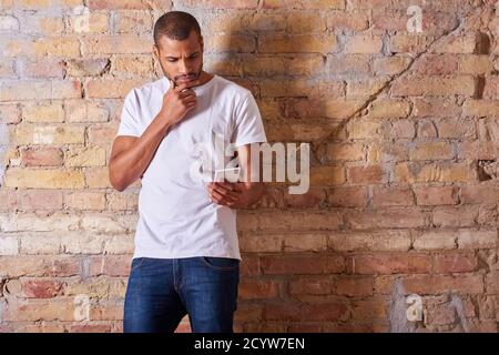 A serious handsome young man using his smartphone in a white tshirt and blue jeans. Stock Photo