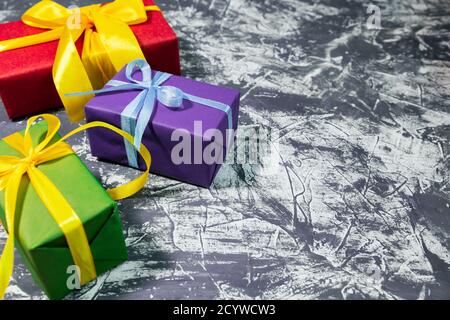 Three stylish multicolored gift boxes with bright ribbons on white and grey background. Space for text. New year concept. Stock Photo
