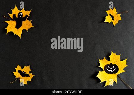 Pumpkin with eyes, Ghost, bats silhouettes made of black paper on yellow maple leaves on a black background. Dark background. Thanksgiving, the Stock Photo