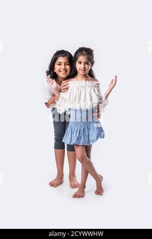 Cute little Indian asian siblings standing and embracing each other in white clothes while standing againstwhite background. Stock Photo