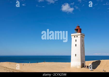 Lighthouse on the dune at Rubjerg Knude, Denmark, on a sunny summer day. Some visitors walking around, others waiting in line to climb up thehistoric Stock Photo