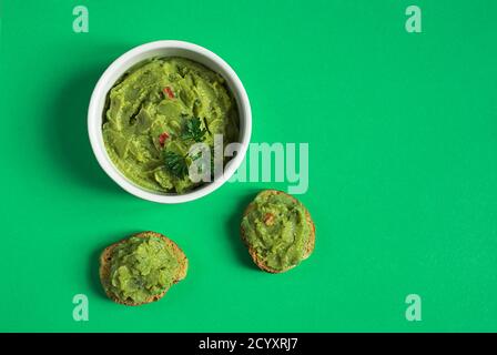 A white bowl and crostini or bruschetta with traditional mexican appetizer guacamole isolated on the green background Stock Photo