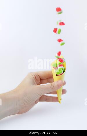 Watermelon jelly beans falling into a paper cone held in one hand Stock Photo