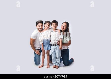 Beautiful Indian young family of four hugging, looking in camera and smiling while standing against white background Stock Photo