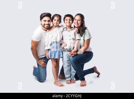 Beautiful Indian young family of four hugging, looking in camera and smiling while standing against white background Stock Photo