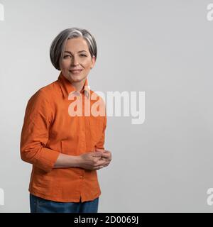 Cheerful woman with gray hair smiles against an isolated background. Woman wearing orange shirt posing in studio. High quality photo Stock Photo