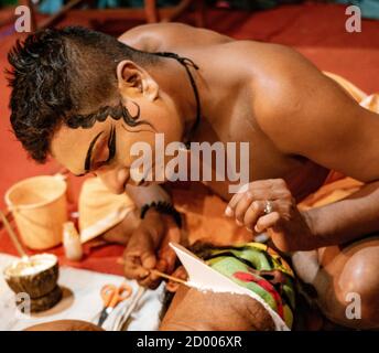 Munnar, India, Mar 11, 2018 - Indian traditional dancer applies paint to the face of a second dancer Stock Photo