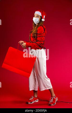 Woman with red hat and package in her hand and a protective mask is covered with garland looking into the distance Stock Photo