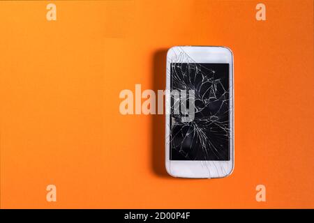 Broken mobile phone with cracked display on orange background, outdoor, natural light. Stock Photo