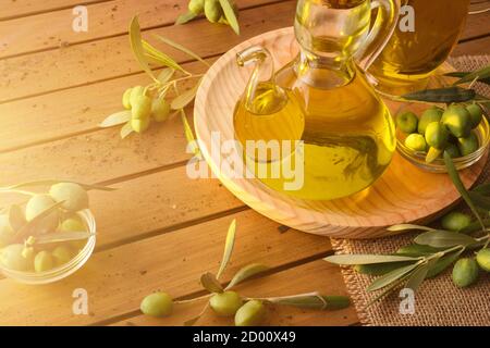 Homemade new harvest olive oil in glass container on wooden table with olives and olive branches. Elevated view. Stock Photo