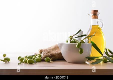 Preparation of olive oil seed in glass for body care and culinary on table with mortar and sack of olives white isolated background. Front view. Stock Photo