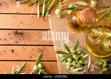 Glass container with olive oil on wooden table with branches and olives in field. Top view. Stock Photo