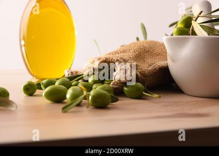 Preparation of olive oil in ceramic glass for body and culinary care on table with mortar and sack of olives. Elevated view. Stock Photo