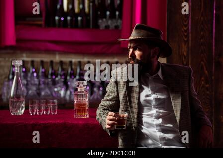 Old traditional whiskey drink - gentlemans beverage. Hipster male with stylish beard drinking beer sitting at the bar. Stock Photo