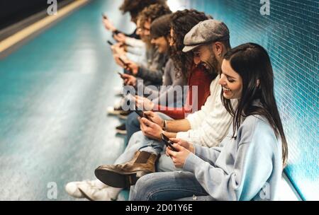 Young people using mobile smartphone while sitting in subway waiting train - Youth millennial addicted to new technology concept Stock Photo