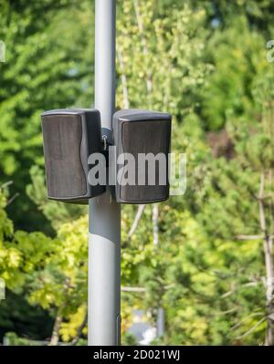 Black speakers suspended from a metal pole with blue sky as a background. Outdoor speakers for music . Stock Photo