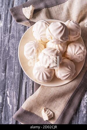 Delicious white marshmallows on white plate, gray napkin, on wooden background, vertical. Stock Photo