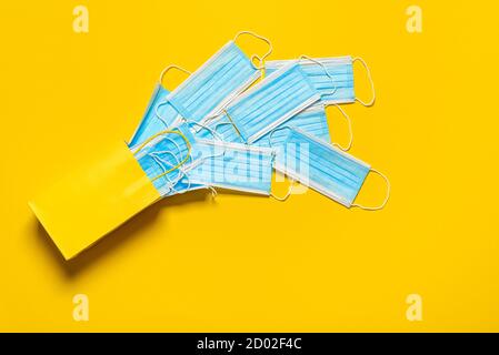 Face masks fallen from a yellow shopping bag, above view. Gift bag with blue medical masks, top view on a yellow-colored background. Stock Photo