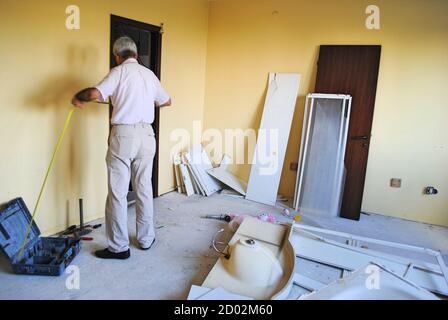 Active mature man doing Interior renovation with measuring tape in hand. House improvement renovation concept. 