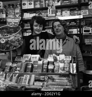 AJAXNETPHOTO. 1970. SOUTHSEA, ENGLAND. - SWEETS AND TOBACCO - MRS CROSS  (RIGHT) PROPRIETOR OF THE CARLTON TOBACCONIST AND SWEET SHOP IN KENT ROAD  WITH HER SON.PHOTO:JONATHAN EASTLAND/AJAX REF:1970 21 Stock Photo