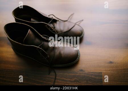 Brown men's boots with untied laces on a wooden floor. Stock Photo