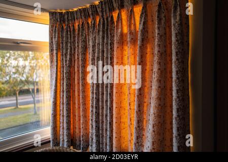 Golden light of a sunset glowing through hanging curtains on one side of a bay window Stock Photo
