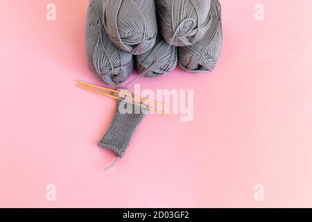 Many gray balls of thread on a PINK background. The threads and knitting needles lie on the background. Home hobby Stock Photo