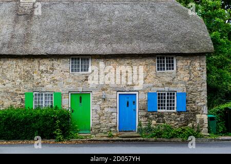 West Lulworth, United Kingdom - 19 July 2020: Beautiful thatched cottage house with blue and green coloured door and shutters, unique Dorset colorfull