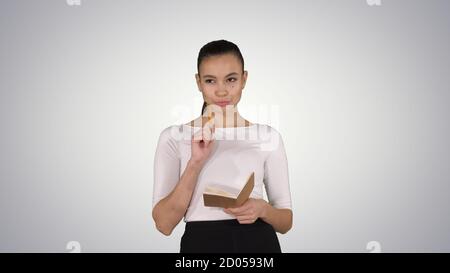 Young woman making notes while walking on gradient background. Stock Photo