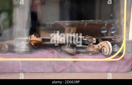 Close up view through dirty show-window on parts of violin as pegboxes and scrolls lying on violet cloth in old shop with stringed instruments. Stock Photo