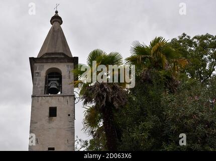 Bell tower of the Church Santa Maria Assunta in Locarno, Switzerland  surrounded by lush green vegetation on the background of slightly overcast sky. Stock Photo