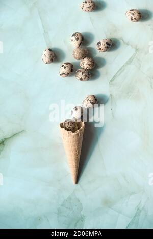 Easter flat lay with quail eggs flying out of waffle ice cream cone. Top view on green stone table. Springtime trendy minimal greeting card concept. Stock Photo
