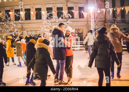 The theme is active recreation in winter on the ice arena. Young caucasian couple happy and in love glide together on an ice rink on christmas evening Stock Photo